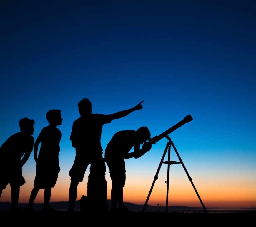 O pai e três filhos olhando através de um telescópio